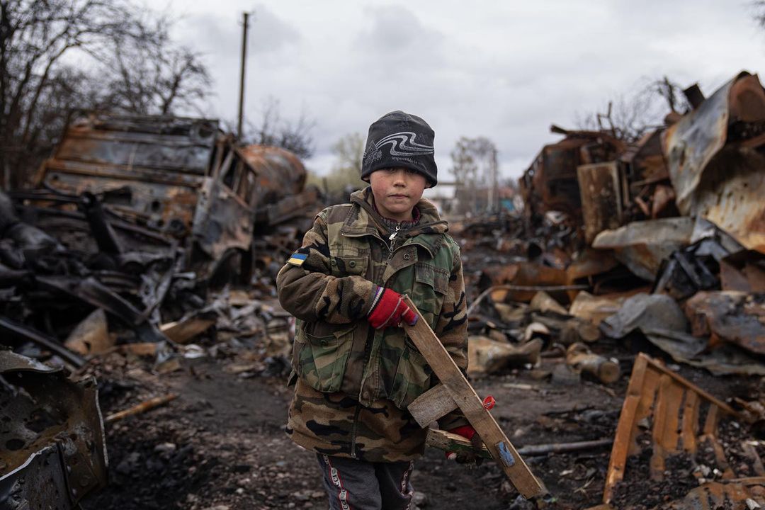 WAR TIME GENERATION 
Yehor, 7, stands holding a wooden toy rifle next to dest...